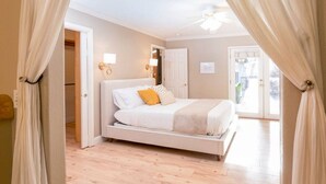Quarto com cama, cortinas, ventoinha no teto e porta.