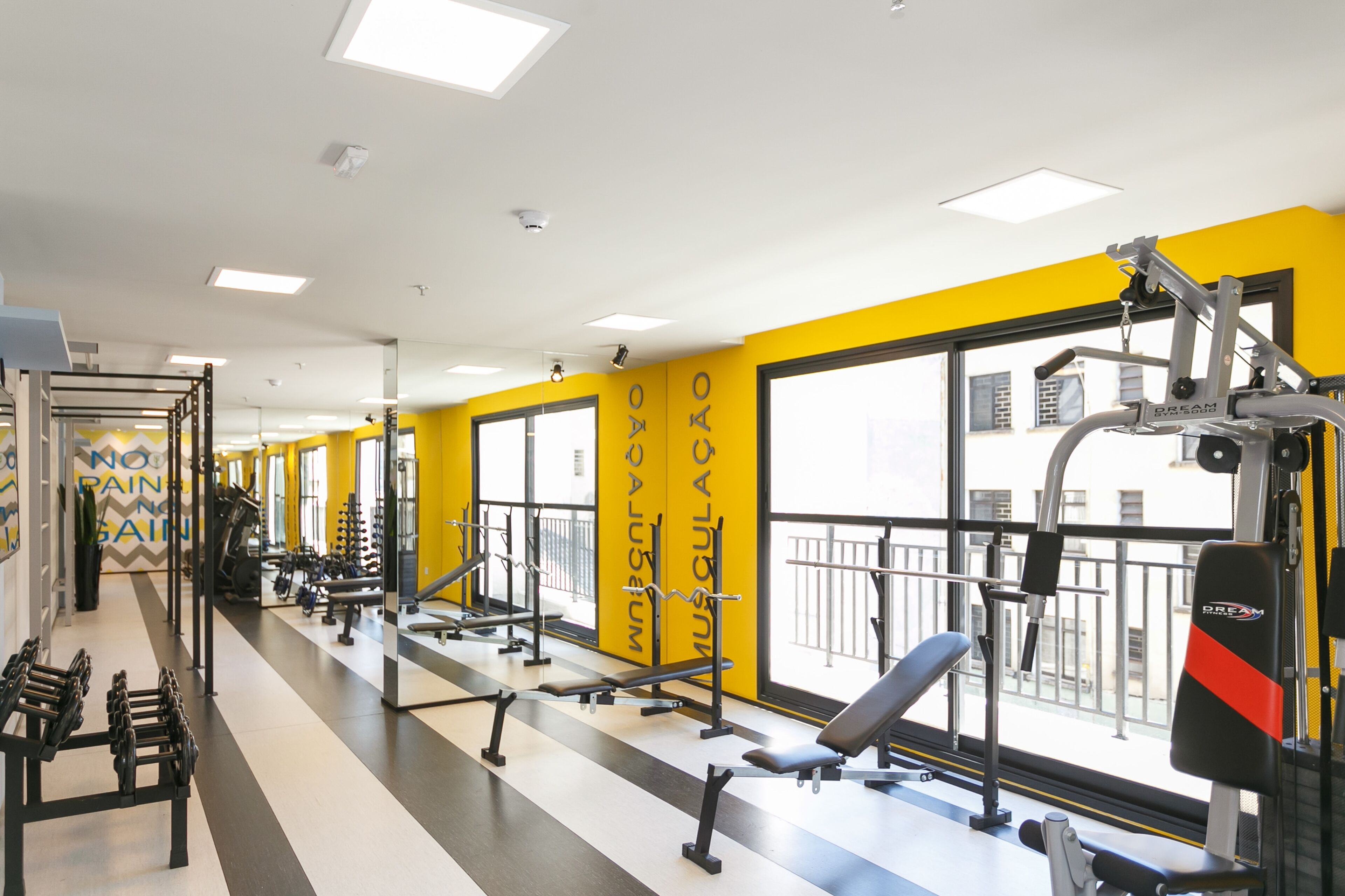 A gym with exercise equipment, large windows, and a yellow and white color scheme.