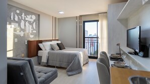 A modern hotel room with a bed, seating area, and a TV.