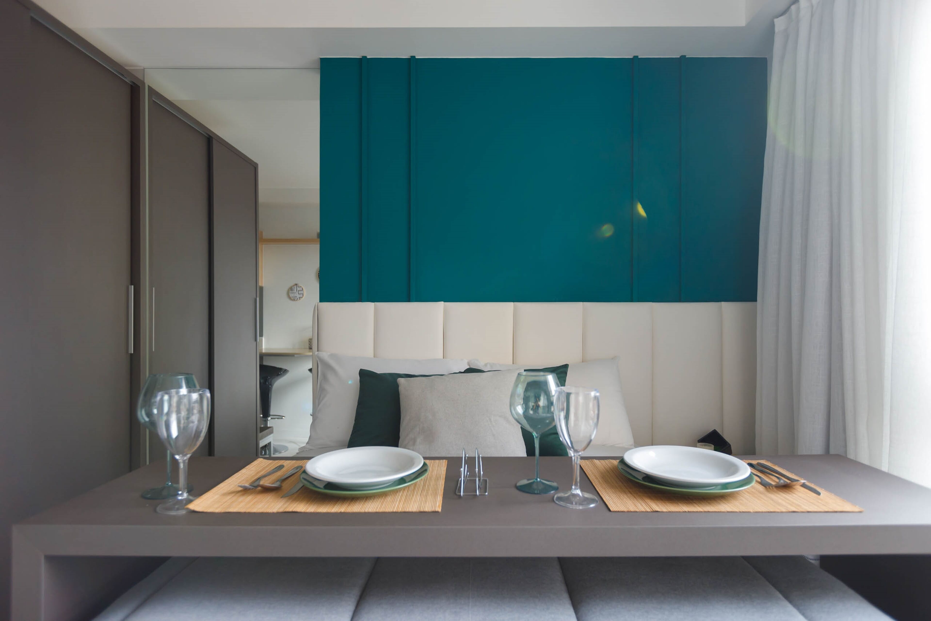 A neatly arranged hotel room with a bed, a dining table set with plates, glasses, and cutlery, and a large teal curtain.