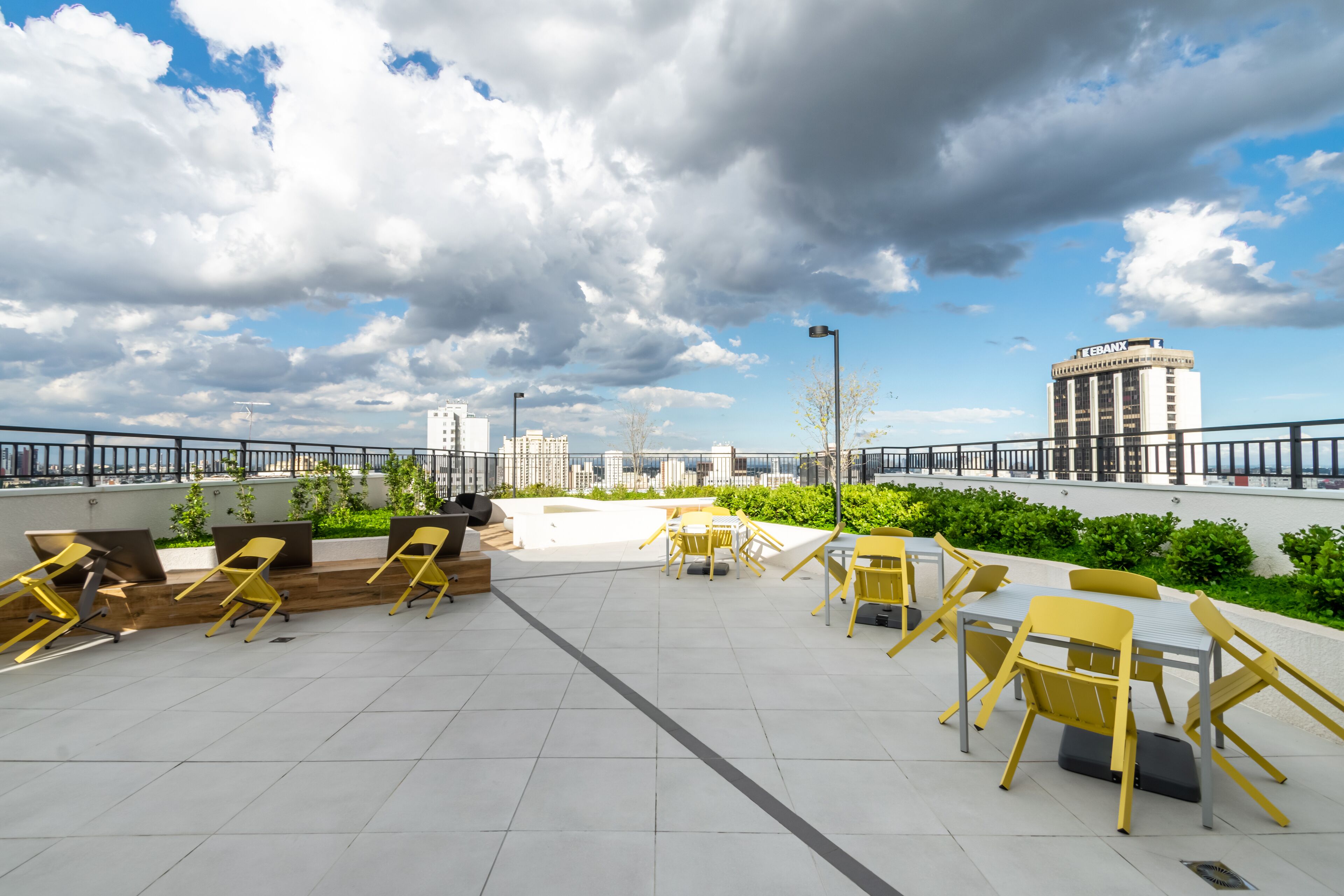 An outdoor seating area with yellow chairs and tables, a view of a cityscape, and a building with 'EBANK' on it.