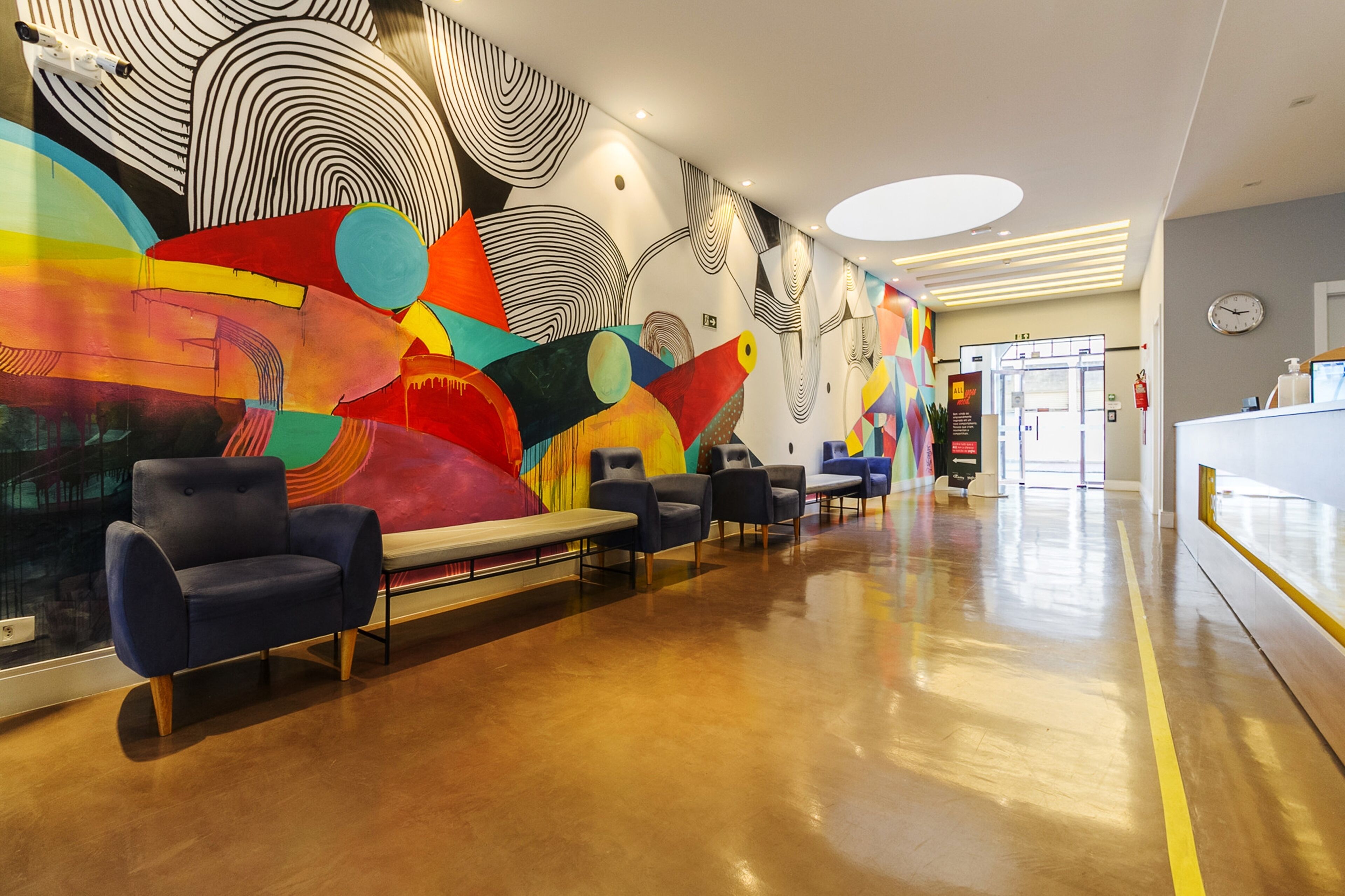 Um lobby moderno com um mural abstrato e colorido, área de estar e balcão de recepção.