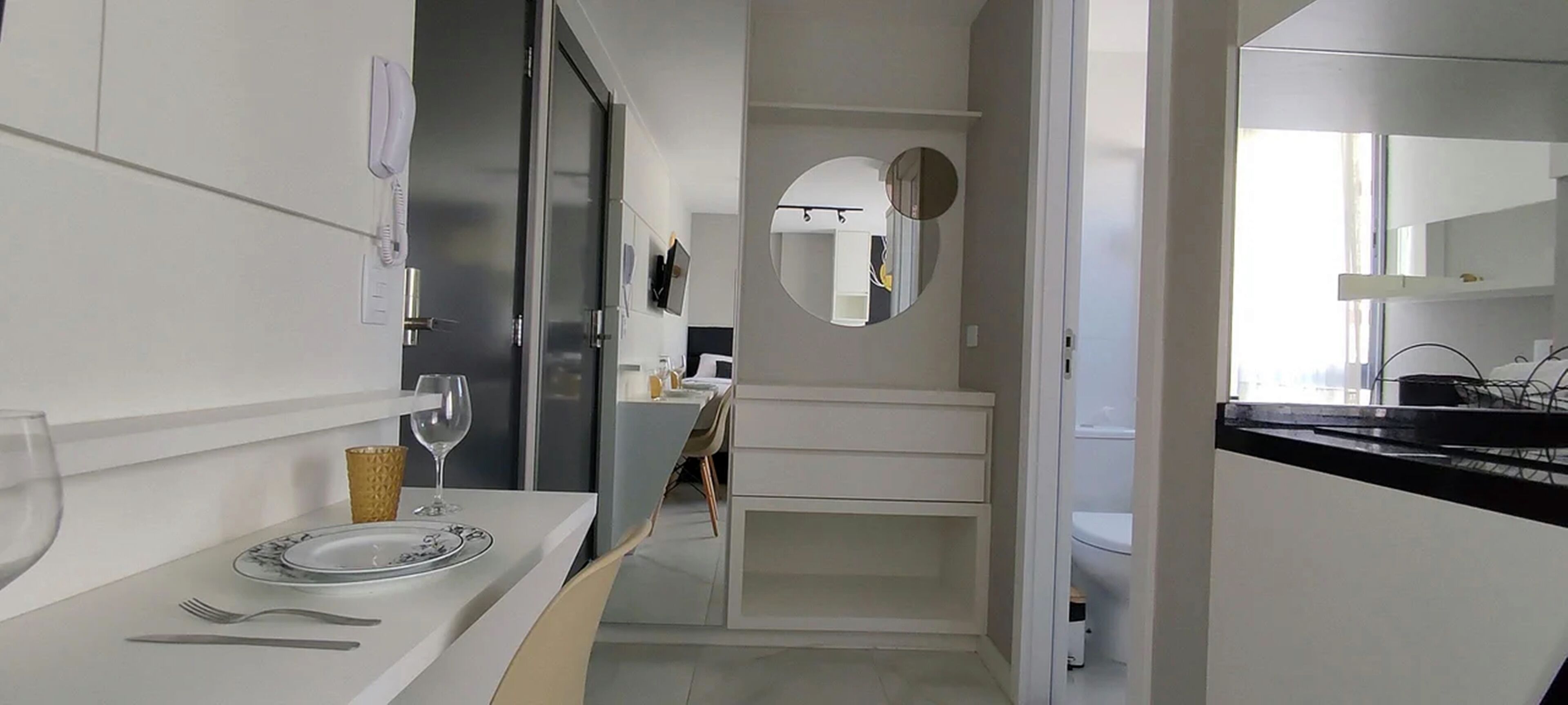 A modern kitchen with white cabinetry, a dining area with a table set for two, and a large mirror above the sink.