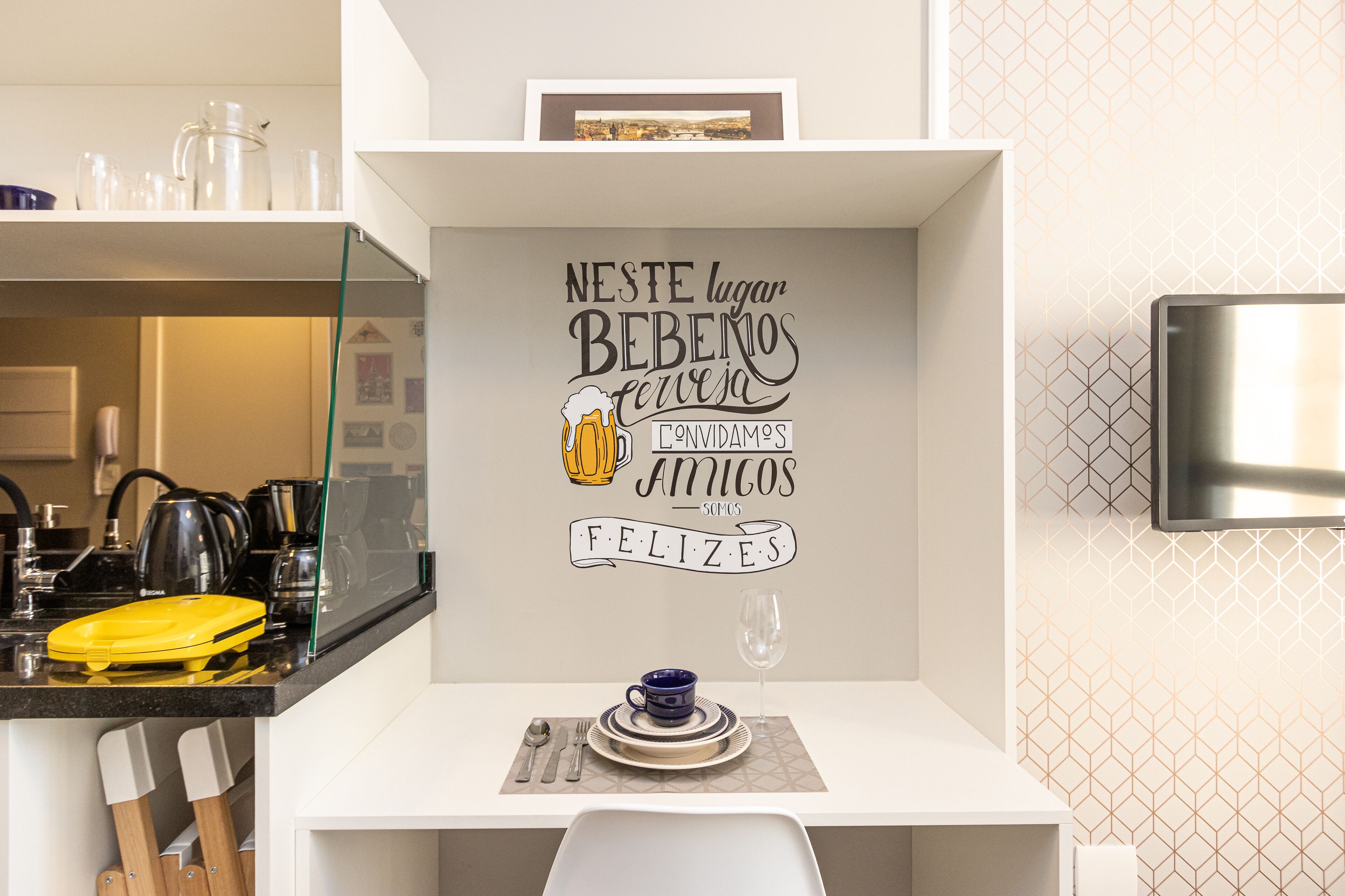 A modern kitchen with a dining area, featuring a wall with a cheerful message, a coffee maker, and a yellow appliance.