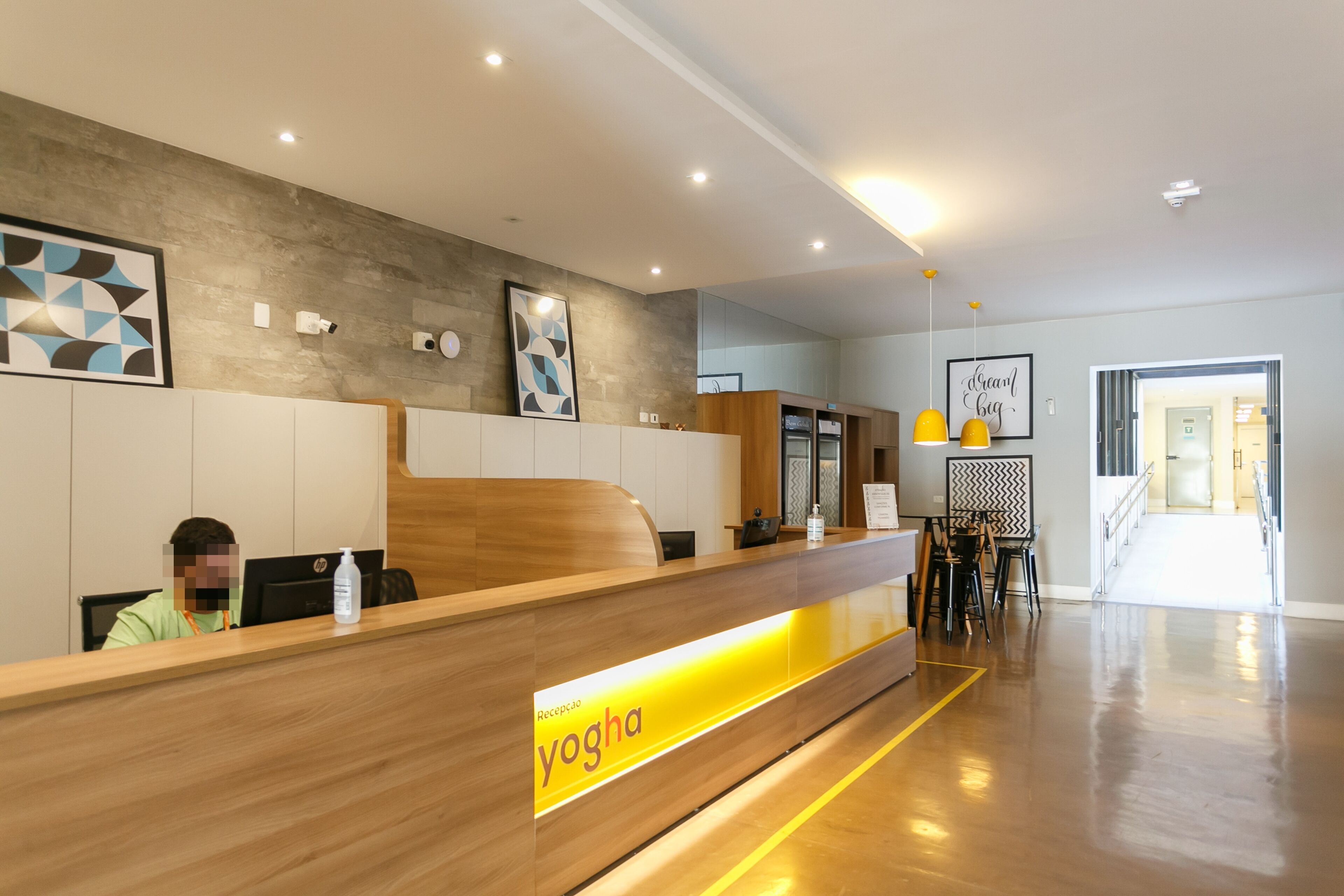 Una zona de recepción con mostrador de madera, una persona sentada frente a un ordenador y un letrero amarillo que dice 
