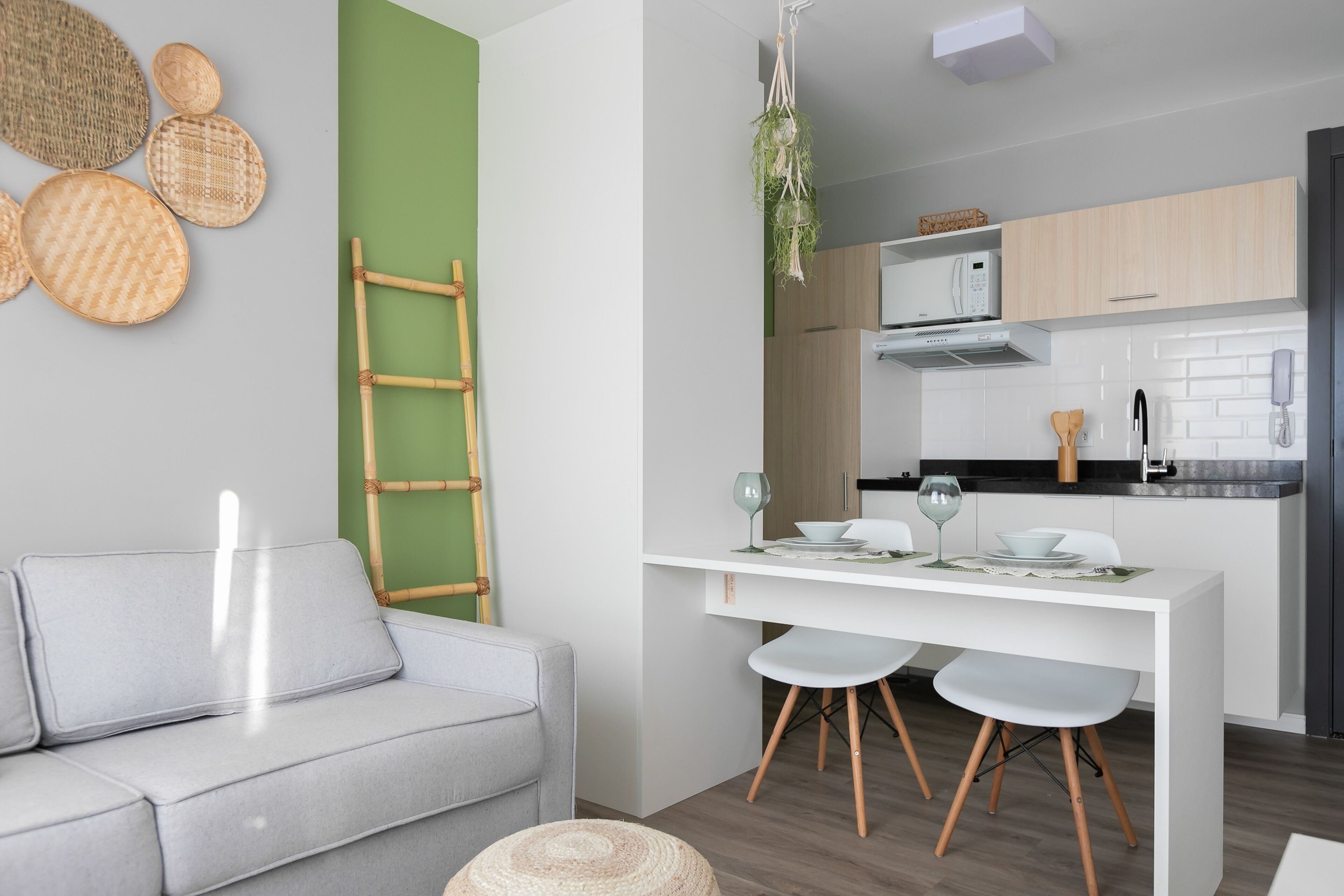 Una cocina moderna con armarios blancos, una mesa de comedor blanca con cuatro sillas y una planta colgante.