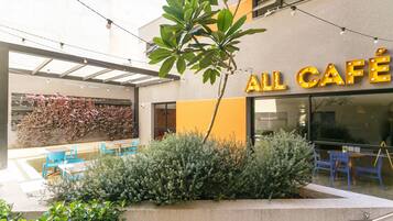 An outdoor café area with a seating arrangement and a building with a sign that reads "ALL CAFÉ".