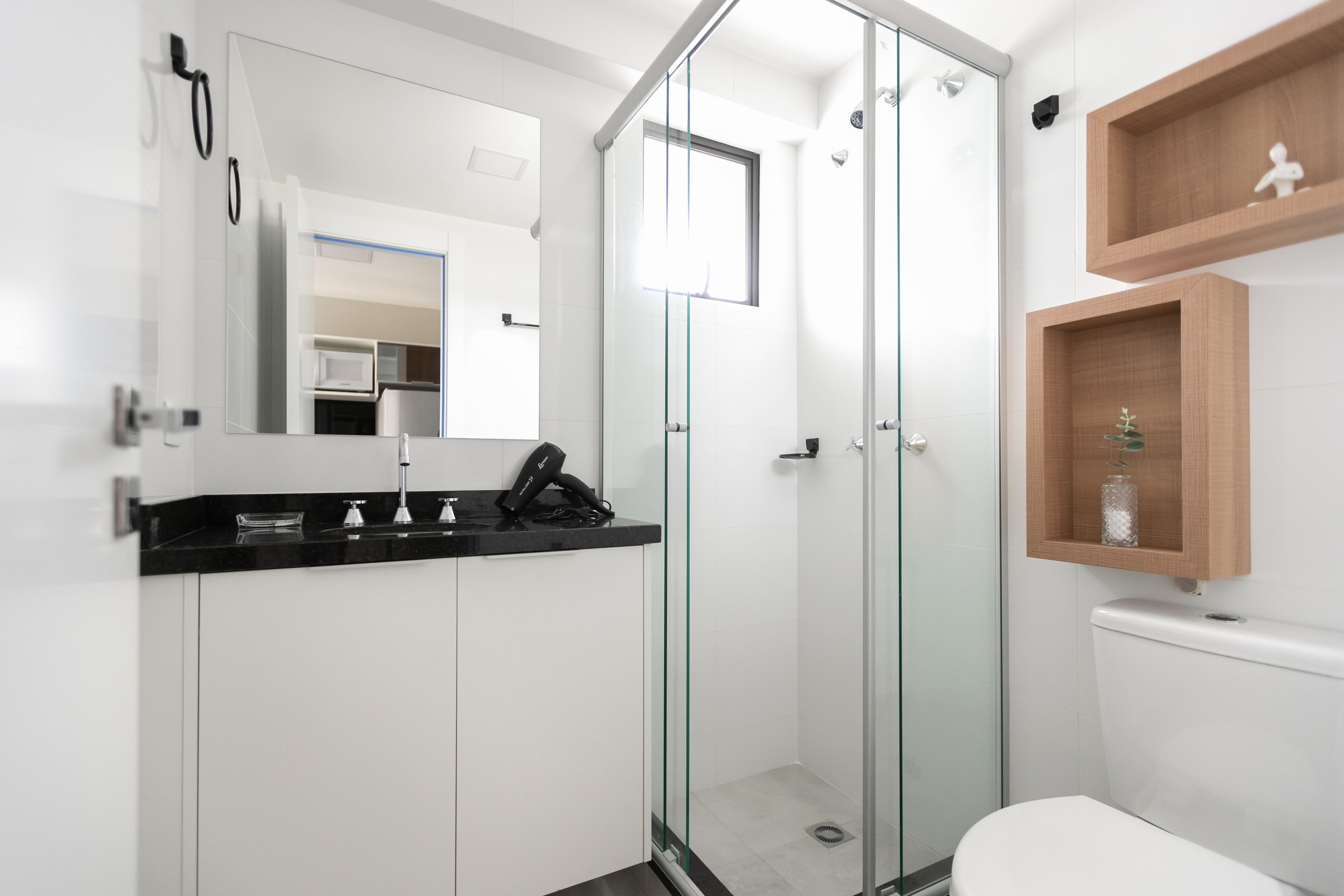 Un baño moderno con ducha envuelta en vidrio, inodoro blanco y encimera negra con un teléfono.