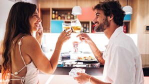 Una pareja brindando con copas de vino en un bar con mostrador y varias botellas al fondo.