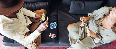 Duas pessoas sentadas num sofá preto com chão vermelho, jogando cartas.