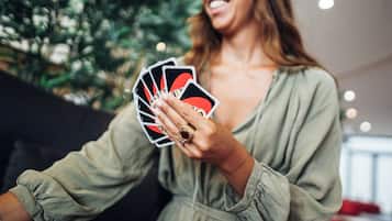 A person holding playing cards in a room with a plant and a red couch.