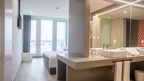 Un baño de hotel moderno con un espejo grande, una bañera y un tocador con lavabo y toallero.