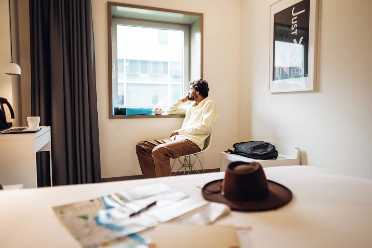 Hotelkamer met een groot raam, een bureau met een laptop, een stoel en een bed met een hoed erop.