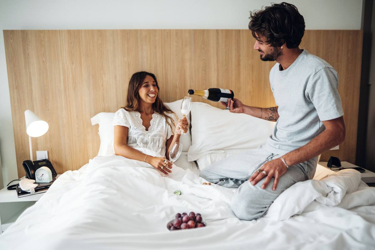 Een hotelkamer met een houten hoofdeinde, een nachtkastje met een lamp, een klok en een mand met druiven.