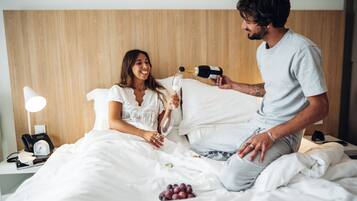 Een hotelkamer met een houten hoofdeinde, een nachtkastje met een lamp, een klok en een mand met druiven.