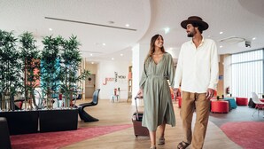 Un moderno vestíbulo de hotel con piso de madera, asientos negros y rojos, y plantas de interior.