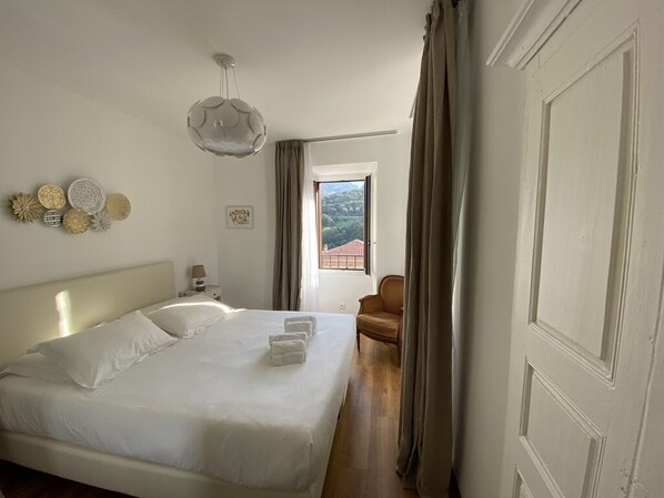 A hotel room with a large bed, a chair, a window with a view, and decorative wall art.