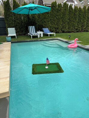 A swimming pool with a small artificial green area marked with an American flag and golf balls, surrounded by lounge chairs and a tiki umbrella. - Pool/5 min walk to Beach/Restaurants/Museums- Village House w/backyard (Sag Harbor)