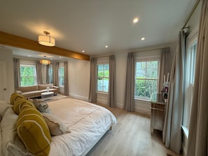 Un dormitorio con una cama grande, una mesita de noche, un aparador y una ventana con cortinas.