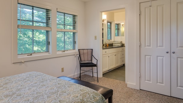 Une chambre à coucher comprenant un lit, une chaise, un bureau, une armoire et une salle de bain avec un miroir et un lavabo.
