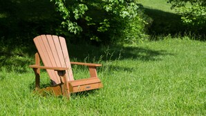 Une chaise Adirondack en bois, placée dans un espace herbeux, avec des arbres en arrière-plan.