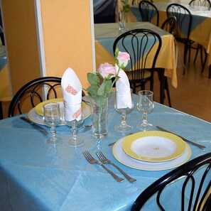 Una mesa de comedor dispuesta con platos, cubiertos, vasos y un jarrón con flores.