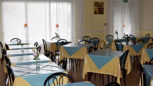 Un comedor con mesas cubiertas con manteles azules y amarillos, sillas negras y centros de mesa florales.