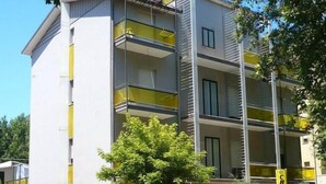 Un edificio de varios pisos con balcones, una entrada con rejas y coches aparcados.