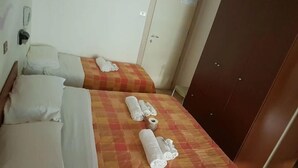 Habitación de hotel con dos camas, cada una con una colcha a cuadros y toallas enrolladas. Se observa un armario y un teléfono instalado en la pared.