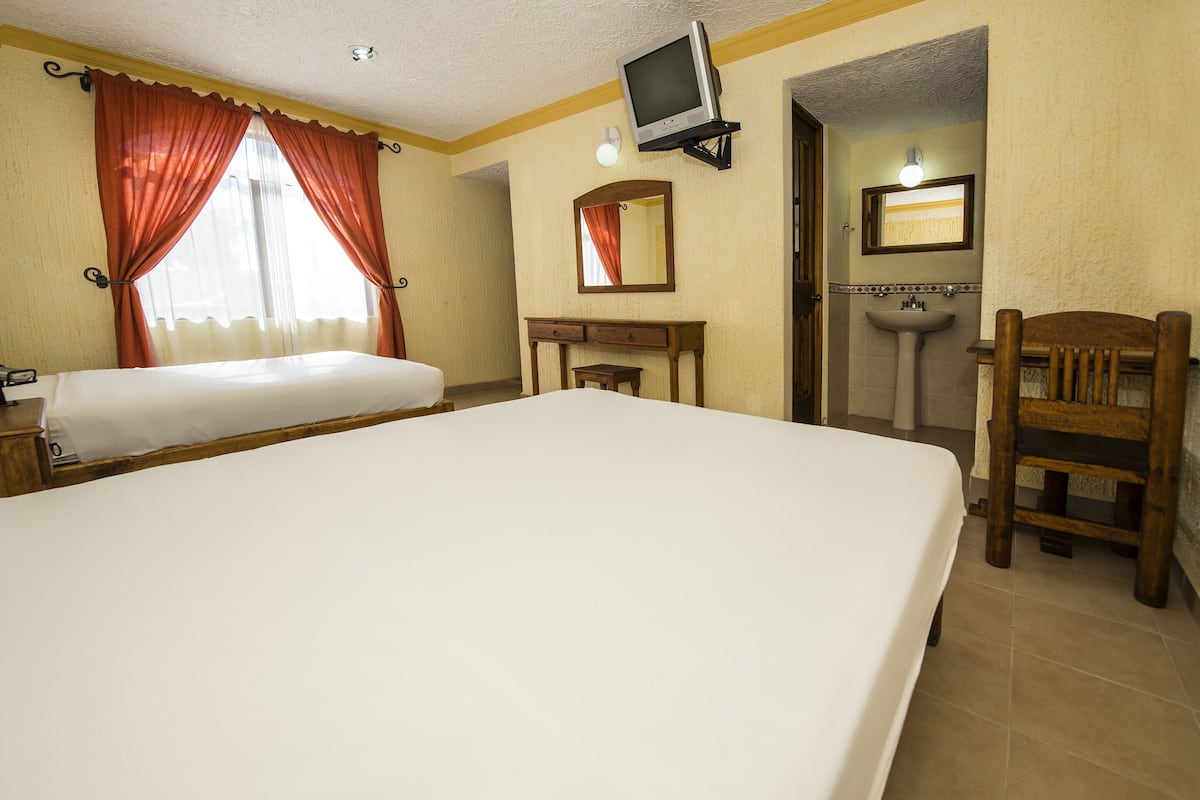 Ein Hotelzimmer mit einem großen Bett, einem Schreibtisch mit Stuhl, einem Fernseher, einem Spiegel und einem Badezimmer mit Waschbecken.
