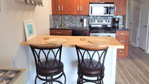 Une cuisine avec des meubles de rangement en bois, un four à micro-ondes, une cuisinière et deux tabourets de bar.
