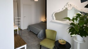 A room with a bed, a chair, a table, a potted plant, a mirror, and a hanging light fixture. - Inkantu B&B (Terrasini)