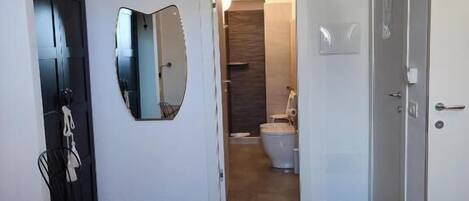Une chambre d’hôtel avec un lit, une chaise, un miroir, une porte et une vue sur la salle de bain.