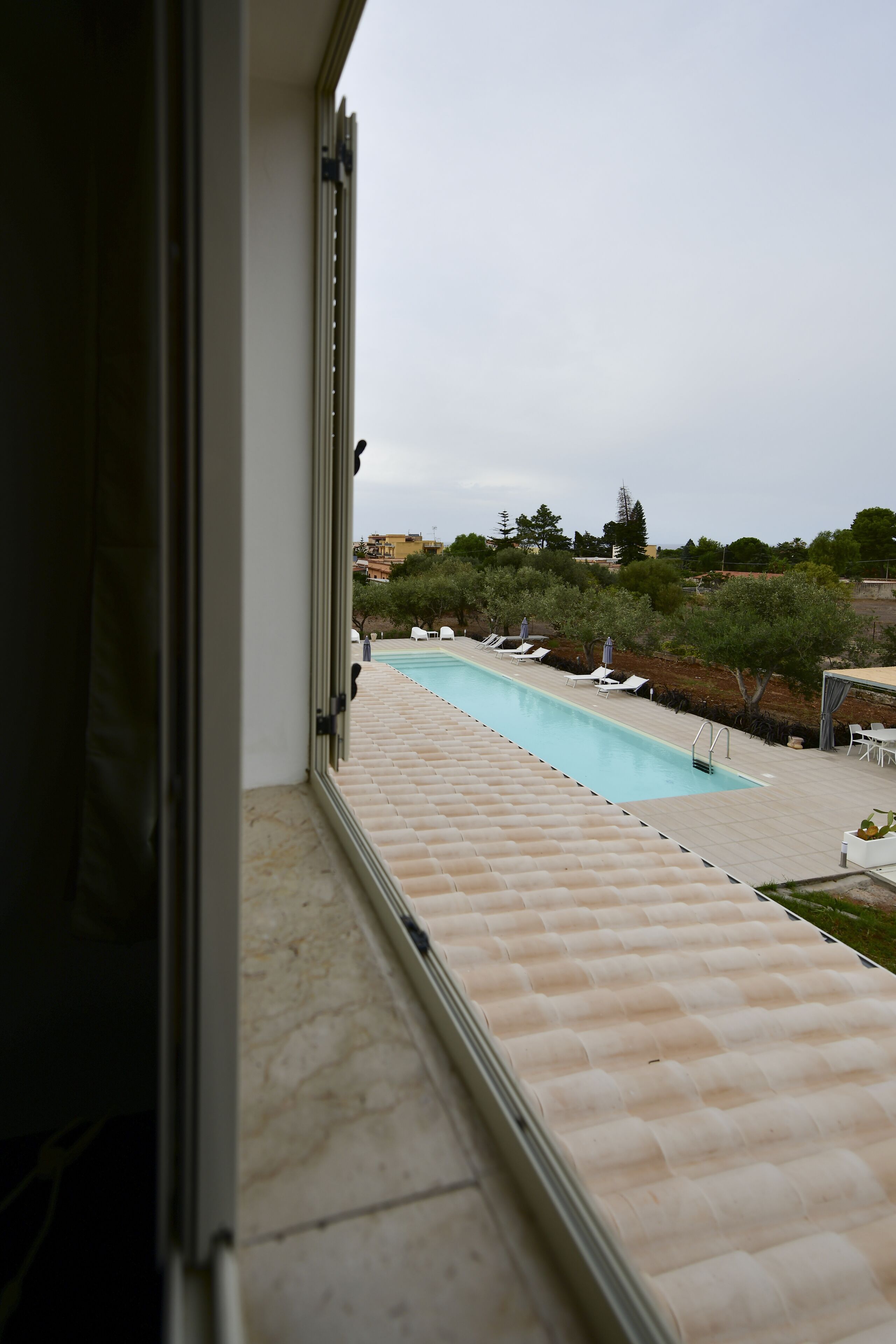 A view of a swimming pool from a window, with lounge chairs and umbrellas along the poolside.