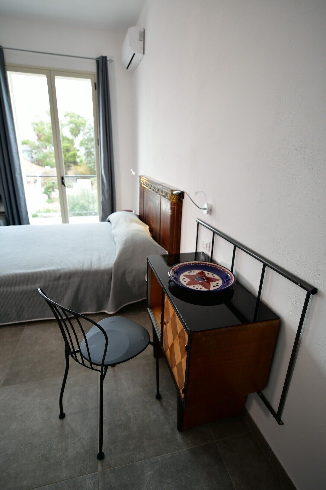 Ein Hotelzimmer mit einem Bett, einem Schreibtisch mit Stuhl, einem Fenster mit Vorhängen und einer Klimaanlage.