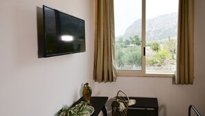 A modern room with a flat-screen TV mounted on the wall, a dining table with a chair, a small bench, and a window with curtains. - Inkantu B&B (Terrasini)