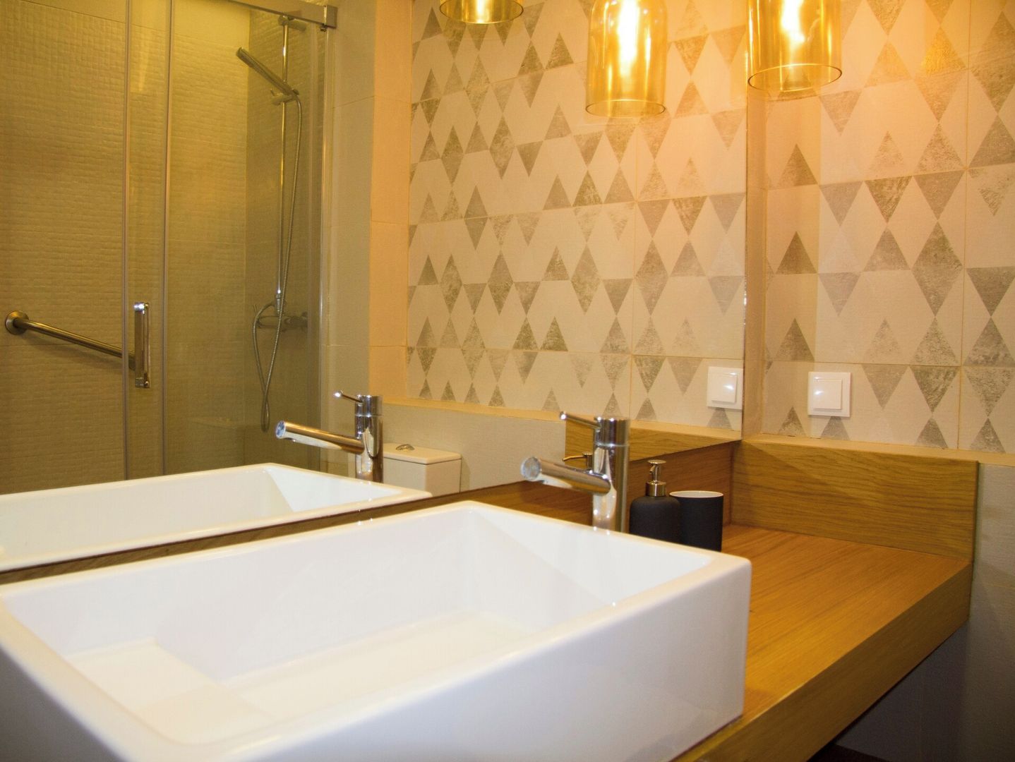 A bathroom with a large white sink, a glass shower enclosure, and a wall with a geometric patterned tile design.