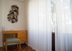 A room with a wooden desk, a bench, and a window with sheer curtains.