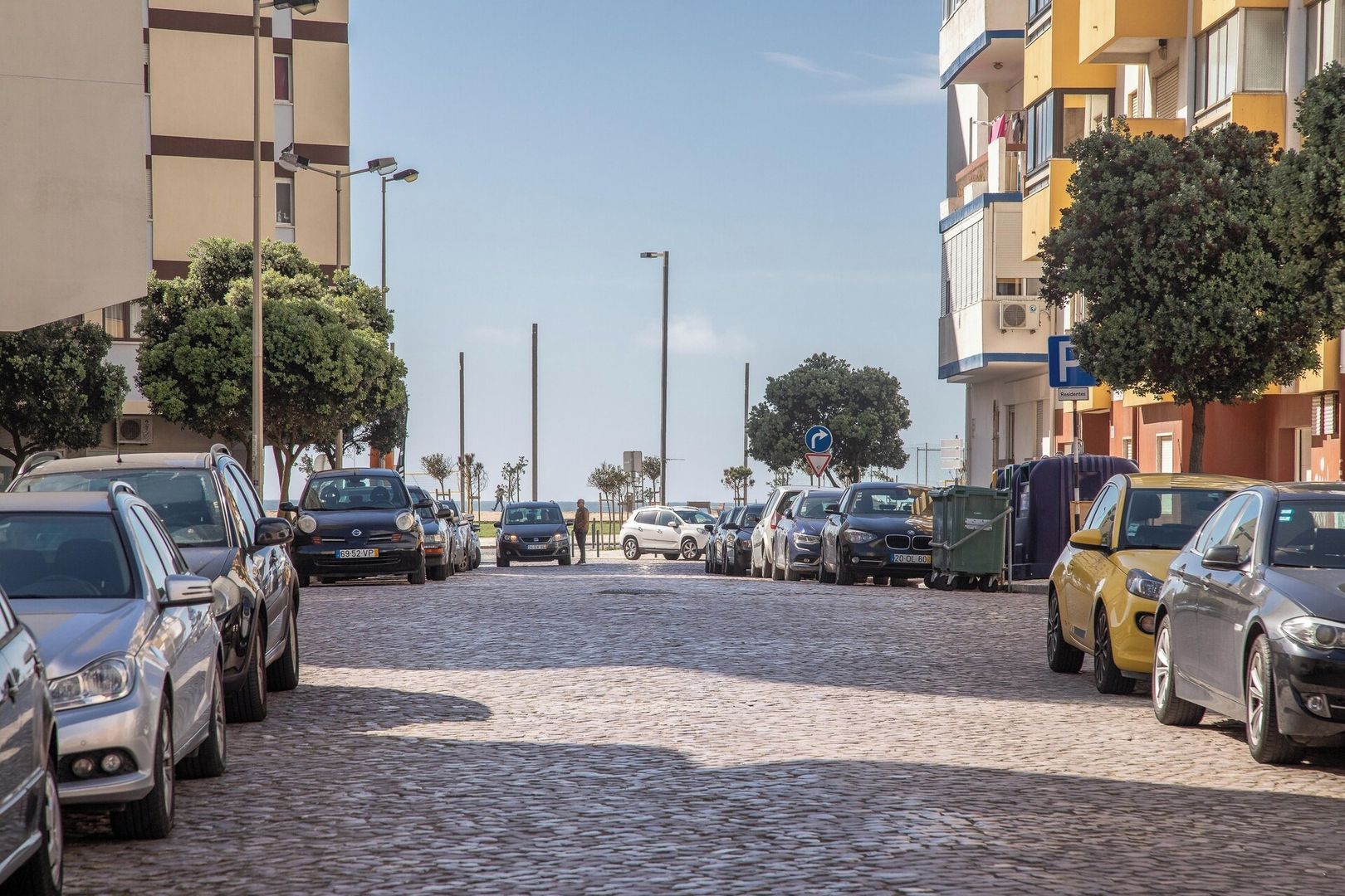 A cobblestone street lined with parked cars and buildings.