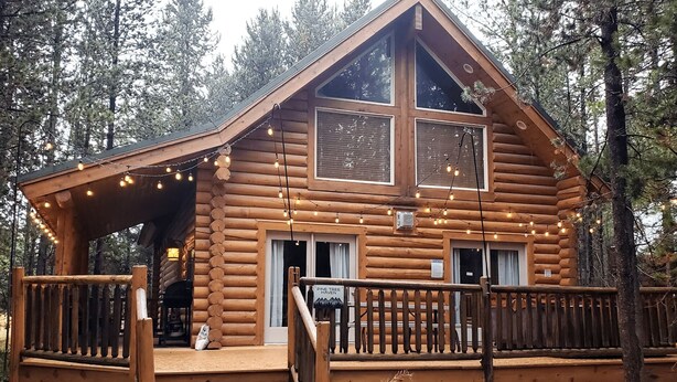 A log cabin with a wooden deck, a staircase leading to the entrance, and a sign indicating it is Pine Tree Haven.