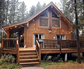 Une cabane en rondins dotée d’une terrasse en bois, d’un escalier menant à l’entrée et d’une enseigne indiquant qu’il s’agit de « Pine Tree Haven ».
