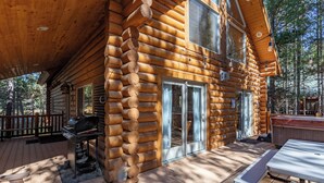 A log cabin with a covered deck, a grill, and a hot tub.