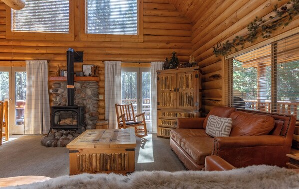 L’intérieur d’une cabane en rondins, avec une cheminée en pierre, des meubles en bois et un coin salon confortable.