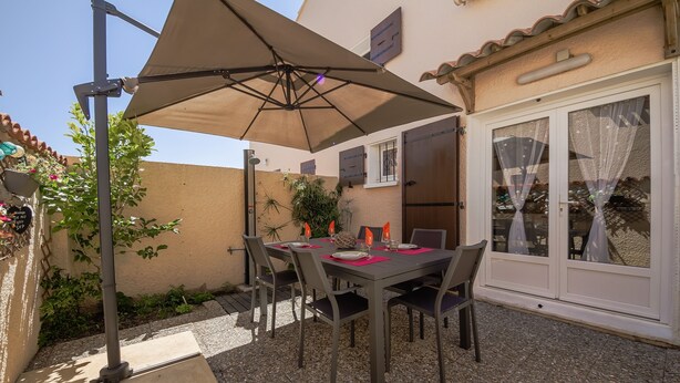 Een terras buiten met een tafel, stoelen, een grote parasol en een deur met ruitpanelen.