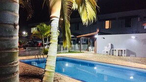 Une piscine aux bords recouverts de pierres, entourée d’une clôture blanche et de palmiers.