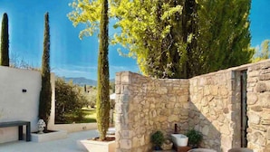 Un patio de piedra con mobiliario exterior, un banco de piedra y plantas en macetas.
