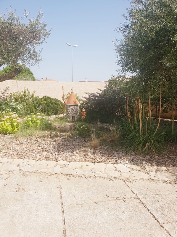 A garden with a stone structure, various plants, and a clear sky.