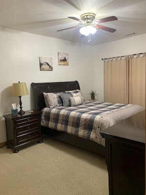 A bedroom with a bed, a nightstand, a lamp, a ceiling fan, and two wall-mounted pictures.