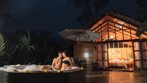 Una pareja en un jacuzzi con una casa de madera al fondo.