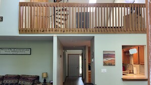 Ein Loft-Wohnbereich mit Schlafgalerie, einer Couch mit gemusterten Kissen, einem Esstisch und einer Küchenzeile mit Holdekor und einer Pendelleuchte.